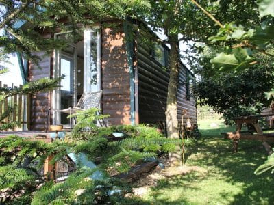 Cabane en bois dans un jardin verdoyant, avec terrasse et chaises confortables.