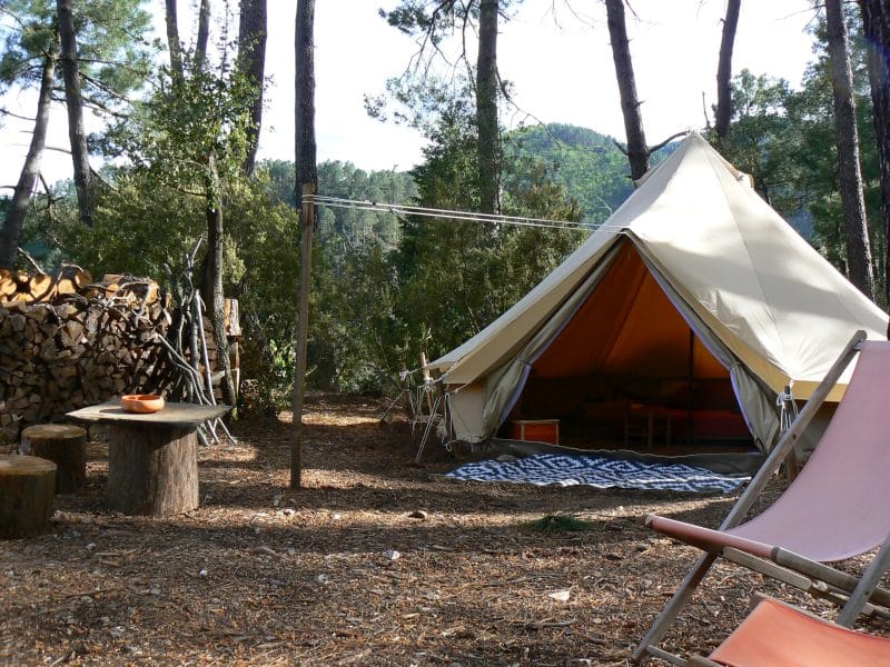 Tente de glamping au milieu des arbres, avec un coin salon en bois.