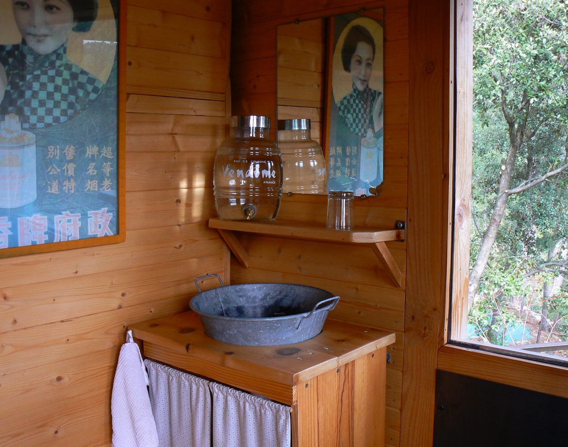 Cabane en bois avec lavabo vintage et affiches rétro, idéale pour un séjour insolite.