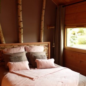 Chalet en bois avec lit douillet, décoré de branches et vue sur la nature.