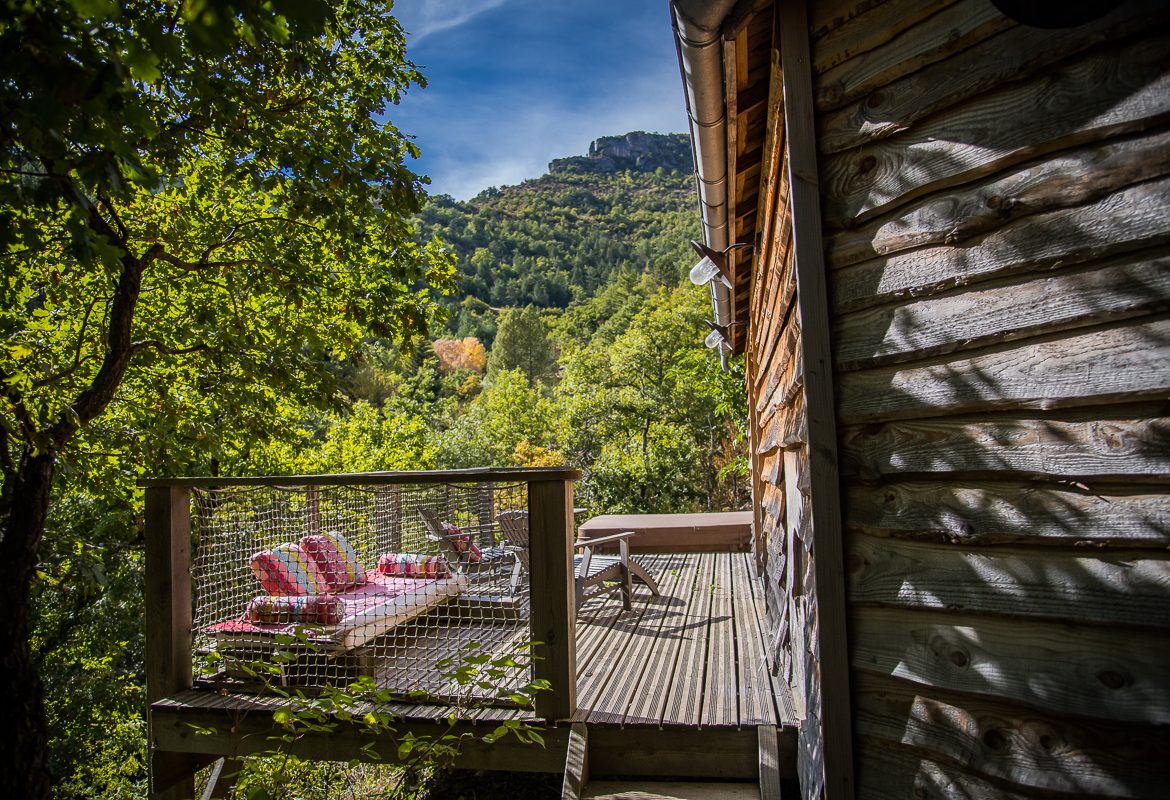 Cabane perchée en bois avec terrasse, vue sur la nature verdoyante.