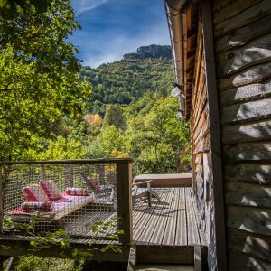 Cabane perchée en bois avec terrasse, vue sur la nature verdoyante.
