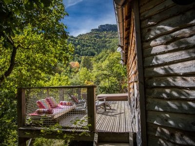 Cabane perchée en bois avec terrasse, vue sur la nature verdoyante.
