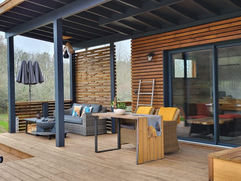 Chalet moderne avec terrasse en bois, mobilier confortable et vue sur la nature.