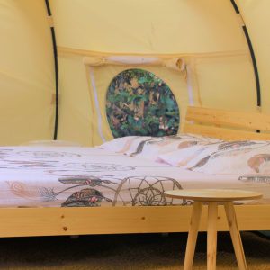 Tente glamping confortable avec lit en bois et décoration naturelle.