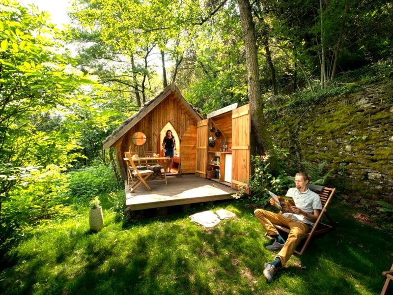 Cabane en bois dans la nature, entourée de verdure, avec terrasse et chaises confortables.