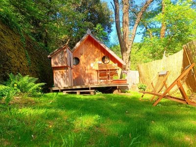 Cabane en bois dans un écrin de verdure, avec chaises longues sur la pelouse.