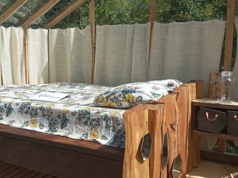 Cabane en bois avec lit confortable et vue sur la nature à travers de grandes fenêtres.