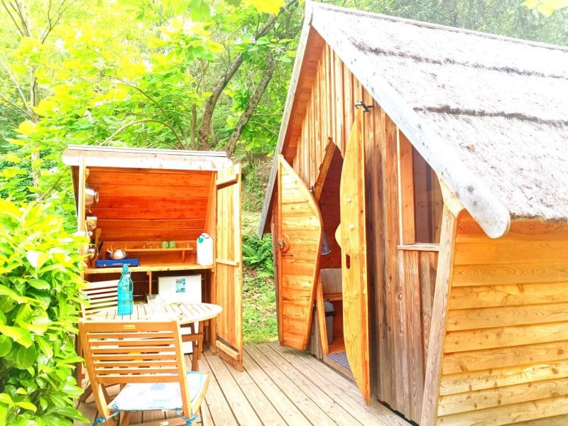 Cabane en bois dans la nature, avec terrasse en bois et espace cuisine extérieur.