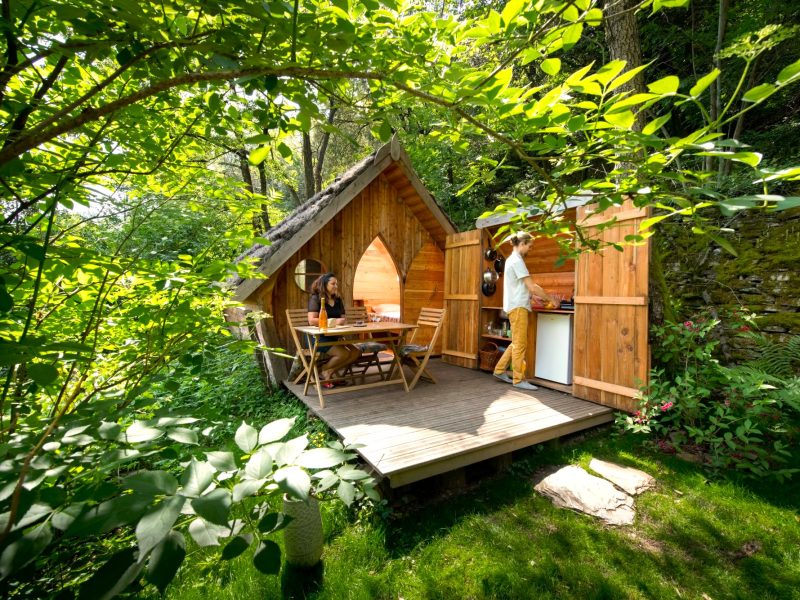 Cabane en bois dans la nature, avec terrasse en bois et verdure luxuriante.