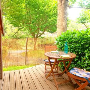 Cabane en bois avec terrasse, entourée de verdure, idéale pour un séjour paisible.