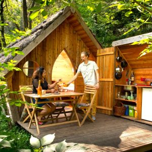Cabane en bois dans la nature, avec une terrasse et une cuisine ouverte.