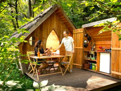 Cabane en bois dans la nature, avec une terrasse et une cuisine ouverte.