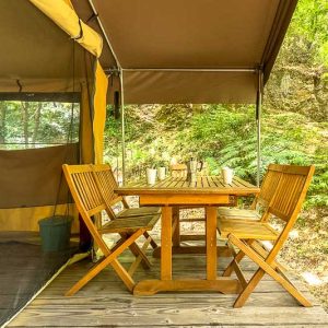 Tente safari en Languedoc-Roussillon avec table en bois et chaises, entourée de verdure.