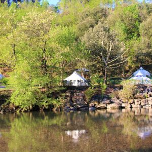 Tentes de glamping au bord dune rivière, entourées de verdure luxuriante.