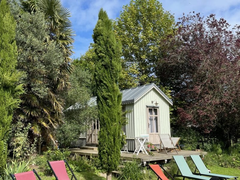 Charmante cabane en bois avec chaises longues colorées dans un jardin verdoyant.
