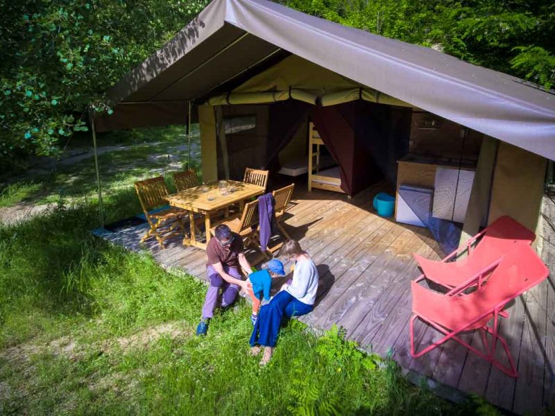 Tente safari spacieuse en pleine nature, avec terrasse en bois et mobilier confortable.