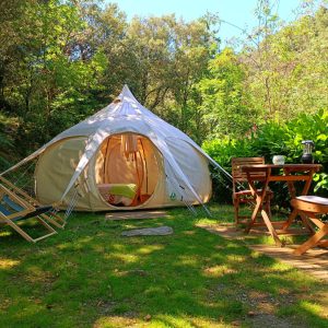 Tente tipi confortable entourée de verdure, avec chaises et table en bois.