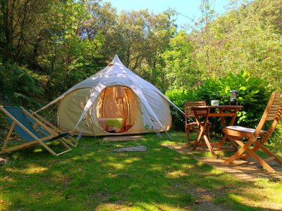 Tente tipi confortable entourée de verdure, avec chaises et table en bois.