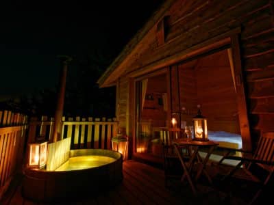 Cabane en bois avec jacuzzi extérieur, éclairée par des lanternes chaleureuses.