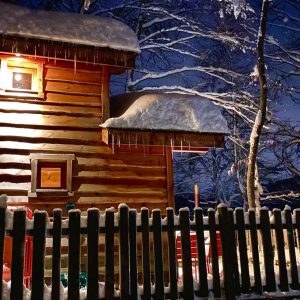 Cabane en bois sous la neige, éclairée par une douce lumière nocturne.