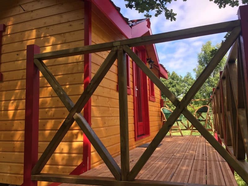 Charmante cabane en bois avec terrasse ensoleillée et chaises confortables.