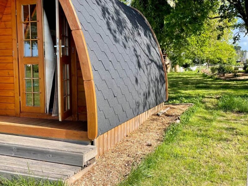 Cabane en bois avec toit en ardoise, située dans un jardin verdoyant.