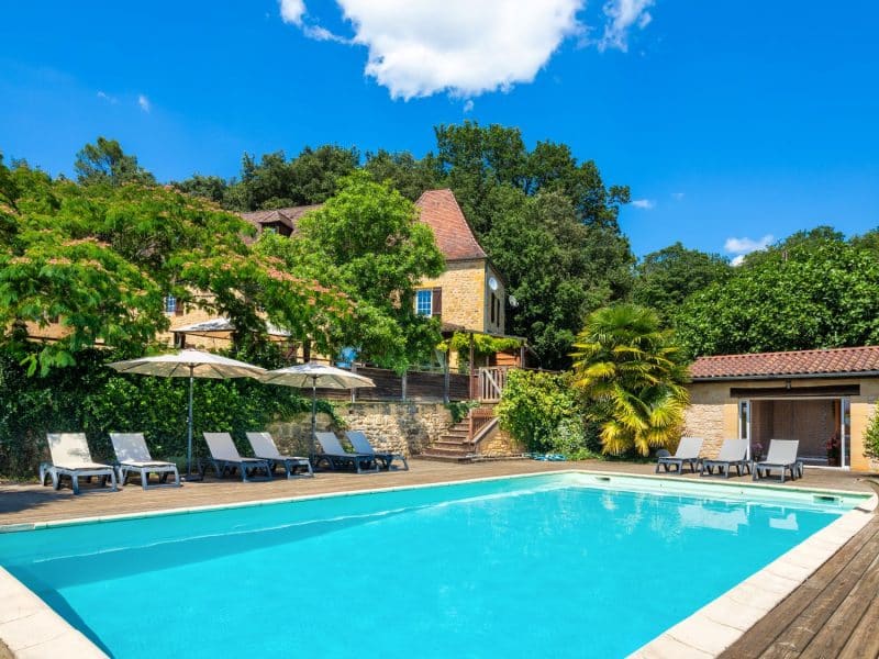 Charmante villa avec piscine, entourée de verdure et chaises longues confortables.