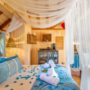 Chalet en bois avec lit décoré de pétales et voilages légers, ambiance cosy.