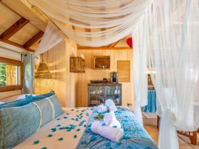 Chalet en bois avec lit décoré de pétales et voilages légers, ambiance cosy.