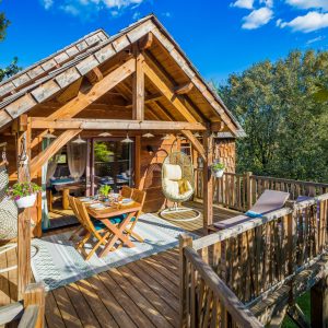 Cabane en bois avec terrasse ensoleillée et chaises suspendues, au cœur de la nature.