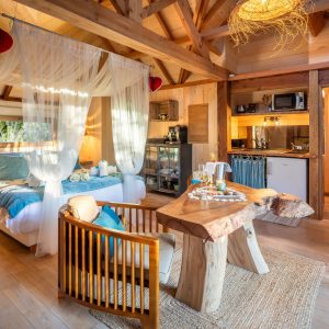 Cabane en bois avec lit douillet, décor chaleureux et cuisine intégrée.