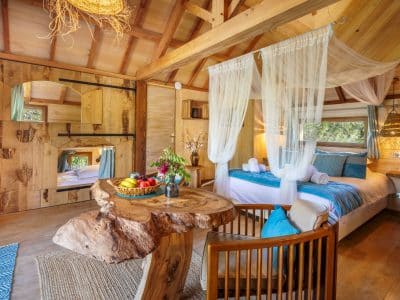 Cabane en bois dans les arbres, décor chaleureux avec lit douillet et table en bois.