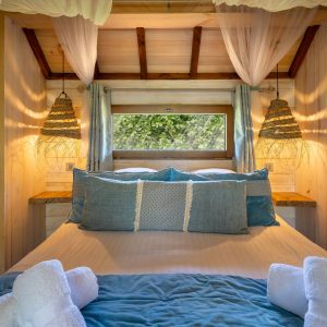 Cabane en bois avec lit douillet, éclairage chaleureux et décor naturel.