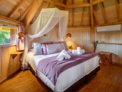 Cabane en bois en Aquitaine, lit douillet avec drap en voile et décor chaleureux.