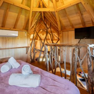 Cabane en bois dans les arbres, intérieur chaleureux avec lit et décor naturel.