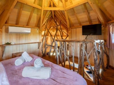 Cabane en bois dans les arbres, intérieur chaleureux avec lit et décor naturel.