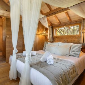 Chalet en bois avec lit douillet, drapés élégants et lumière naturelle.