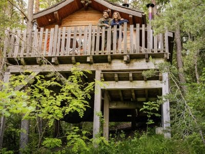 Cabane perchée en bois entourée darbres, offrant une vue imprenable sur la nature.