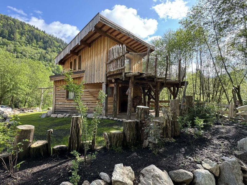 Cabane en bois perchée, entourée de verdure et de montagnes majestueuses.