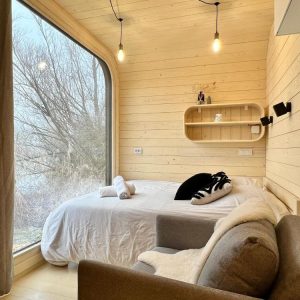 Cabane moderne en bois avec grande fenêtre et lit douillet, vue sur la nature.