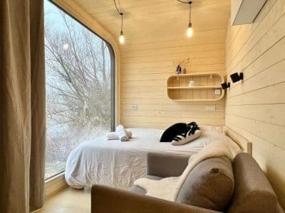 Cabane moderne en bois avec grande fenêtre et lit douillet, vue sur la nature.