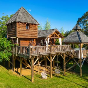 Cabane perchée en bois avec terrasse, entourée de verdure en Aquitaine.