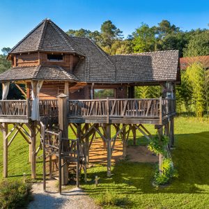 Cabane perchée en bois avec terrasse, entourée de verdure en Aquitaine.