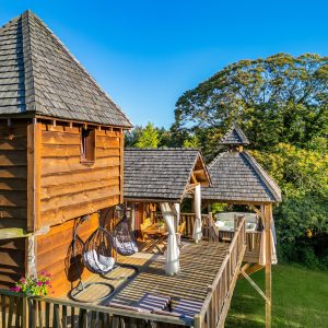 Cabane perchée en bois avec terrasse et hamacs, entourée de verdure en Aquitaine.