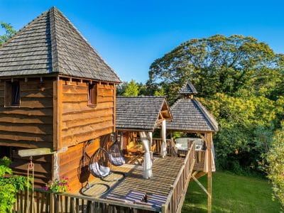 Cabane perchée en bois avec terrasse et hamacs, entourée de verdure en Aquitaine.