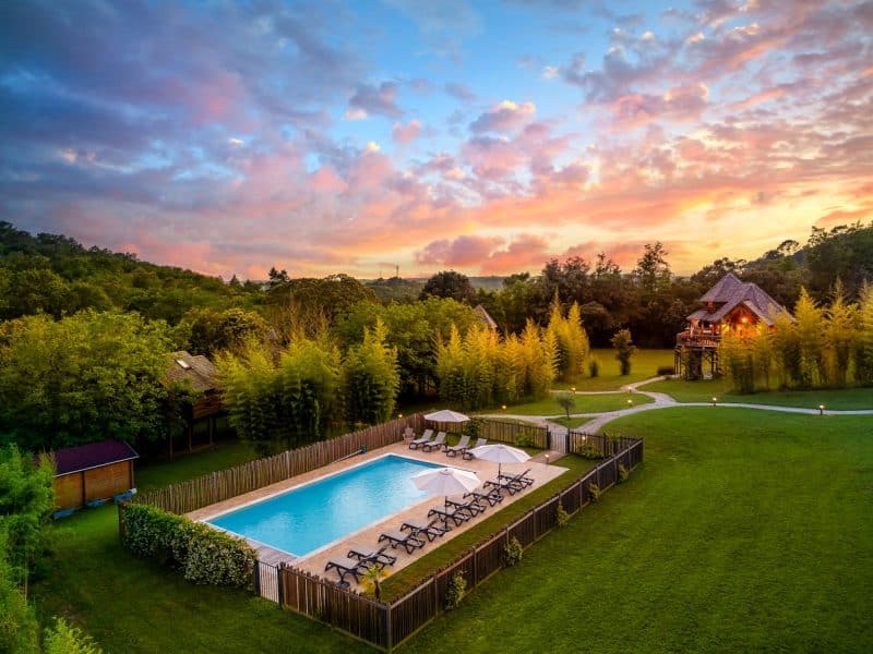Charmante villa avec piscine, entourée de verdure et dun ciel coloré au coucher de soleil.