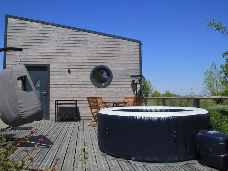 Cabane moderne avec jacuzzi sur la terrasse et vue dégagée sur la nature.