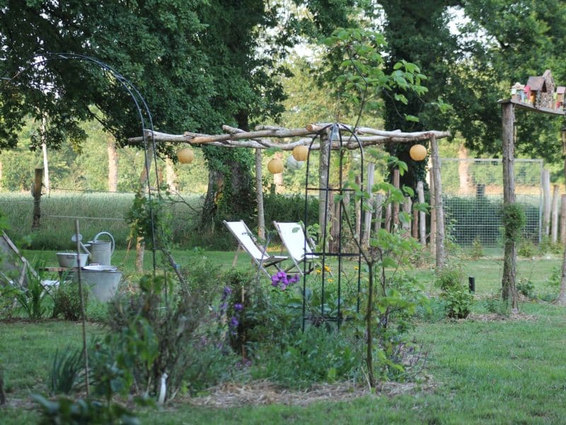 Gîte rural avec un jardin verdoyant et des chaises longues sous des arbres.