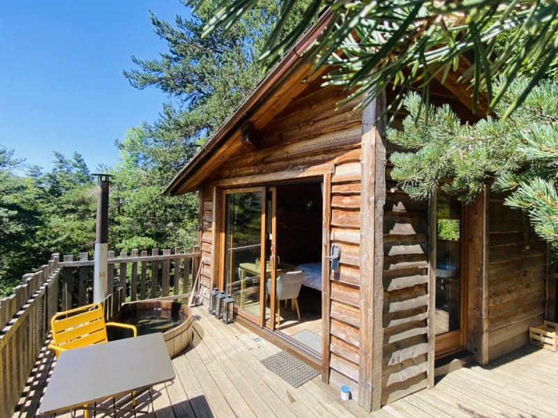Chalet en bois avec terrasse ensoleillée et vue sur la nature environnante.